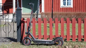 E-Wheels E2S V3 GT Pro parkerad bredvid ett rött staket med röd stuga i bakgrunden