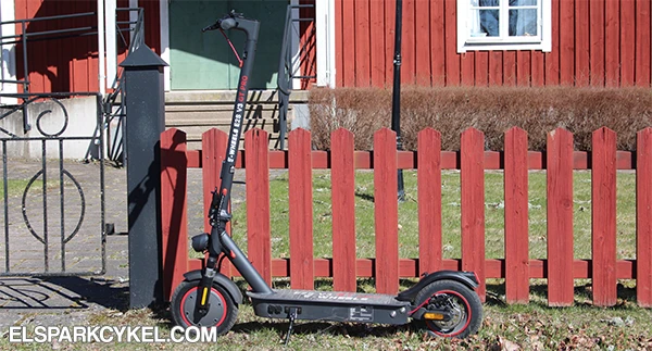 E-Wheels E2S V3 GT Pro pysäköity punaisen aidan viereen punainen mökki taustalla