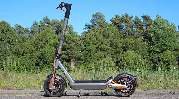 Xiaomi Electric Scooter 6 Max parkeret langs vej i sommersolen med skovbevoksning i baggrunden
